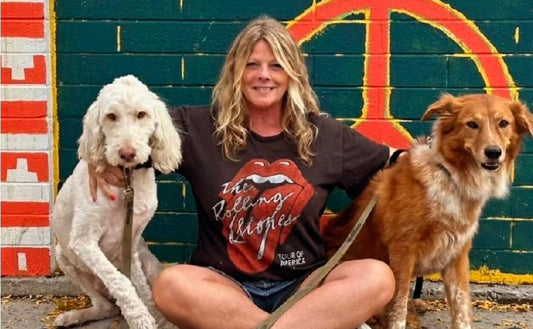 Laurie, founder of LOVEDOG, sitting with her two dogs in front of a colorful mural in Scottsdale
